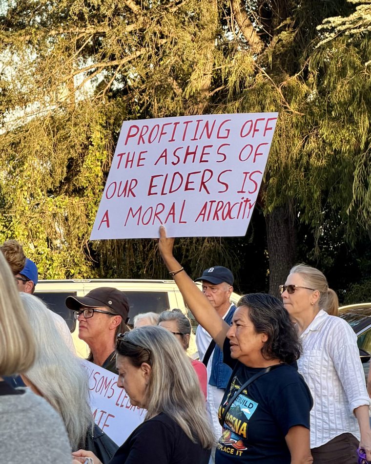 A protester holds a sign reading 'Profiting off the ashes of our elders is a moral atrocity' at an Altadena rally.